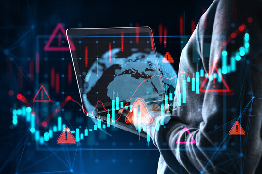 Hooded person using laptop with global market charts, warning icons, glowing data analytics on a dark abstract background for cybersecurity risk.