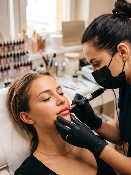 Professional aesthetician performing lip blush permanent makeup on young woman