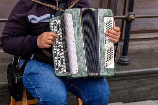 Street Musician Playing a Green Button Accordion. Seated street musician playing a green button accordion beside stone steps and a metal railing in an outdoor urban setting.