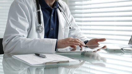 Doctor taking notes on a clipboard and holding a digital tablet, combining traditional paperwork...