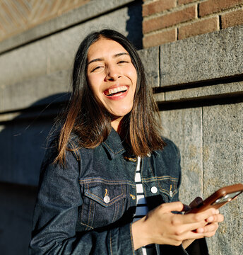 Portrait of a happy young woman tourist travelling or student or a businesswoman entrepreneur, using a smartphone phone or texting outdoors in front of a modern urban background
