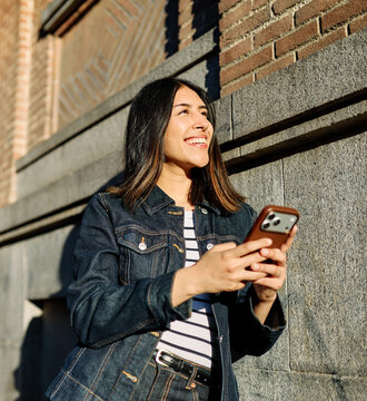 Portrait of a happy young woman tourist travelling or student or a businesswoman entrepreneur, using a smartphone phone or texting outdoors in front of a modern urban background