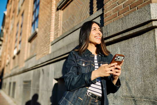 Portrait of a happy young woman tourist travelling or student or a businesswoman entrepreneur, using a smartphone phone or texting outdoors in front of a modern urban background