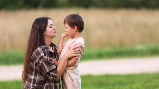 Slow motion shows young mother comforting her upset autistic son in nature. She strokes his hair and kisses his forehead. Gentle scene expresses support compassion and unconditional love.