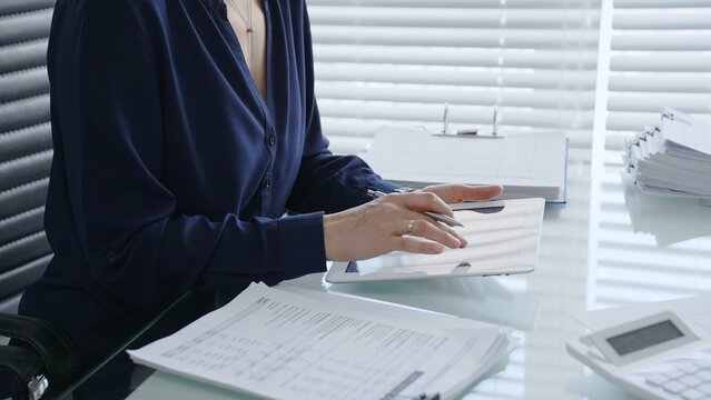 Professional woman using digital tablet for business tasks, typing data and reviewing documents at a modern office desk, symbolizing efficiency and financial management