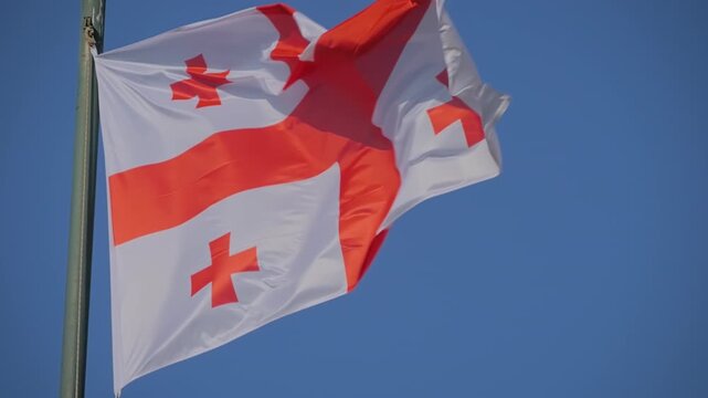 Colorful Georgian flag is fluttering in the wind against clear blue sky in Georgia - slow motion. Freedom, diplomacy, politics, patriotism, and international affairs concept