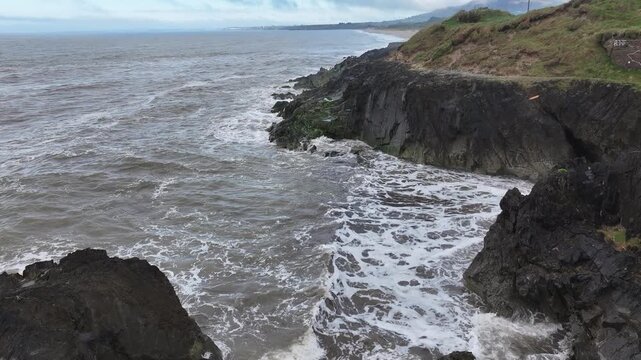 Aerial view of stormy waves crashing against rugged rocky coastline of the Irish Sea