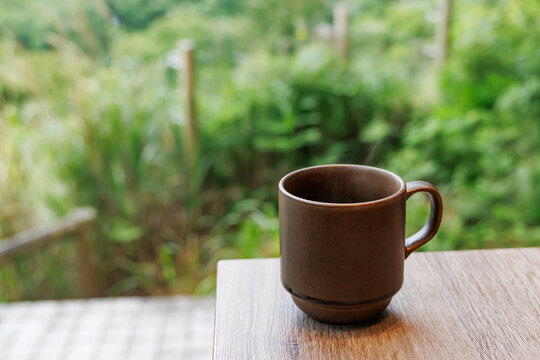 緑豊かな背景と木目テーブルの上のマグカップに入ったホットコーヒー