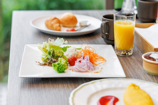 テーブルに配置されたサラダとオムレツとジュースの朝食セット