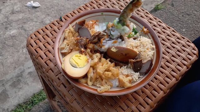 Chicken porridge with a full complement of toppings: shredded chicken, a hard-boiled egg, chicken liver and gizzard, and a sprinkle of peanuts. A favorite Indonesian street food for breakfast