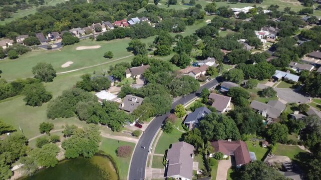 Onion Creek Club fairways surround residential cul de sacs near Pebble Beach Dr in Austin suburban neighborhoods. Tree lined cart paths loop through suburban backyards, Travis County, Texas