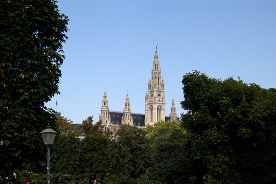 La maestosa torre neogotica del Municipio di Vienna Rathaus che svetta sopra gli alberi del parco Rathauspark con passanti lungo il sentiero in una giornata estiva, Austria.