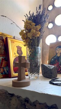 Orthodox Icons and Cross in Church Interior. Orthodox Christian icons and wooden cross displayed on a windowsill in a church or monastery interior with dried flowers and stone wall.