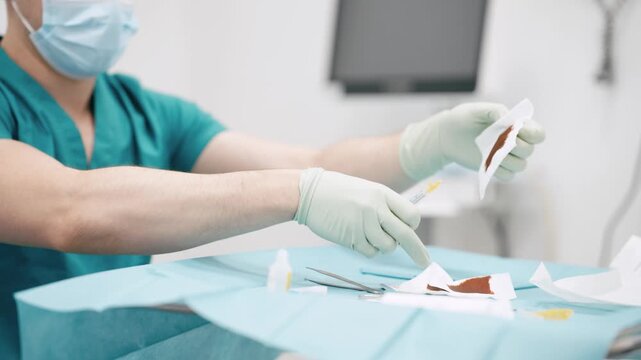 Male doctor in surgical mask and sterile gloves preparing a syringe with iodine solution before a medical procedure in a hospital room
