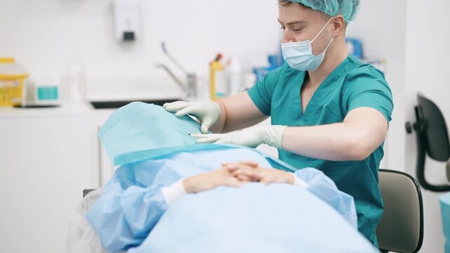 Male surgeon in scrubs and mask placing a sterile drape on a female patient's face, preparing her for a medical procedure in a clinic