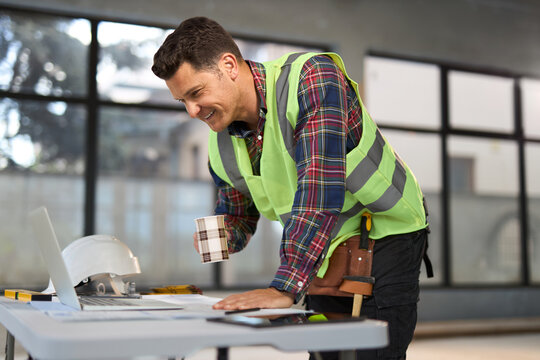 Happy civil engineer working on a computer at construction site.