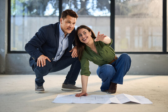 Young happy couple talking while analyzing housing plans at construction site.