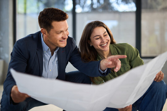 Young happy couple talking while analyzing housing plans at construction site.