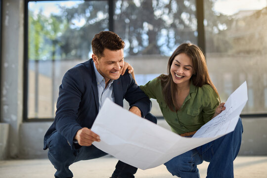 Young happy couple talking while analyzing housing plans at construction site.