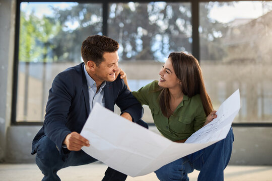 Young happy couple talking while analyzing housing plans at construction site.	