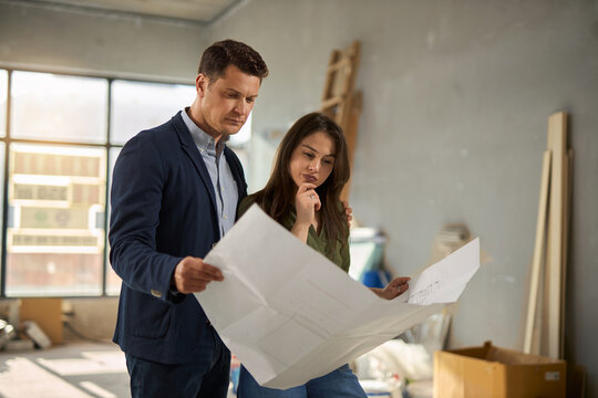 Young couple cooperating while reading blueprints of their developing house. 