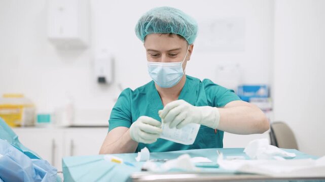 Professional male surgeon in sterile gloves and uniform preparing medical tools and gauze for an operation in a modern hospital clinic