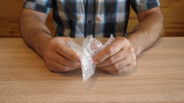 A man crumples bubble wrap in his hands, creating a distinctive crackling sound while squeezing it. The video contains clean original audio.