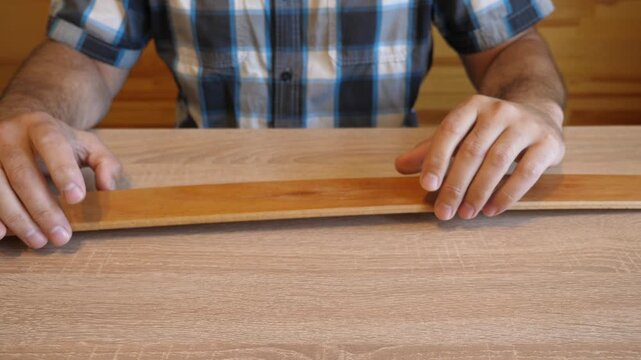 A man rotates a wooden slat in his hands, tapping it on the table surface. The video contains clean original audio.