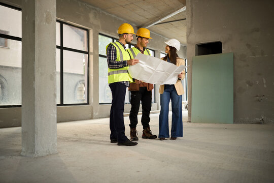 Female building contractor  and manual workers cooperating while working on blueprints at construction site