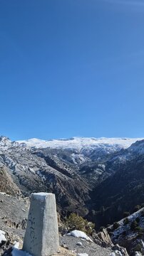 Young woman recording a selfie video while trekking on a sunny winter day. Majestic snowy mountain panorama of Sierra Nevada in Spain