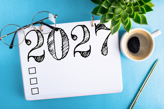 New year resolutions 2027 on desk. 2027 goals list with notebook, coffee cup, plant on blue table. Resolutions, plan, goals, action, checklist, idea concept. New Year 2027 resolutions. Copy space