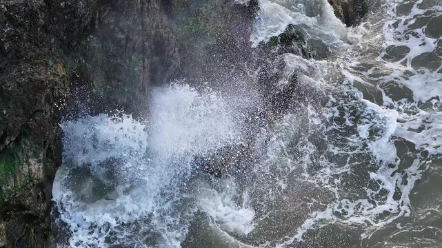 stormy Irish Sea waves crashing at rugged Clones Rocks with powerful spray from blowhole fountain