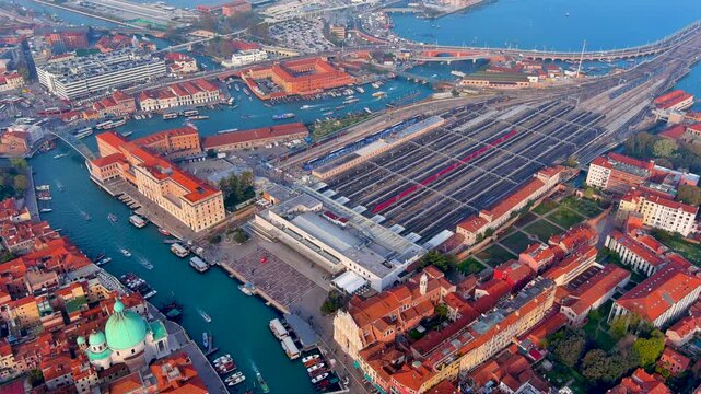 Aerial drone view of Venezia Santa Lucia railway station with trains and platforms by the Grand Canal, vaporetto boats, bridges and the San Simeone Piccolo church dome, Venice, Italy.
