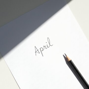 White paper with April written in elegant script accompanied by a pencil and natural shadow perfect for spring themes planning or monthly concepts