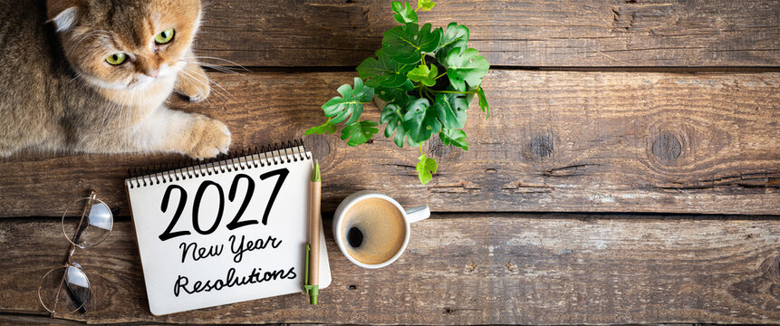 New year resolutions 2027 on desk. 2027 resolutions list with notebook, coffee cup, cute cat on table. Goals, resolutions, plan, cozy, hygge concept. New Year 2027 background