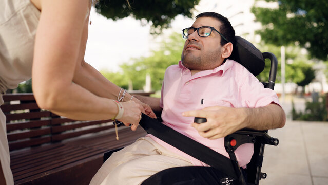 Caregiver securing a seatbelt for a man with spina bifida in his electric wheelchair, offering support and inclusion outdoors