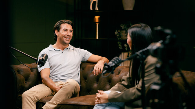 Two content creators recording a podcast, man speaking into microphone with woman host during audio broadcast