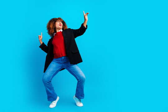 Joyful young woman dancing energetically against a bright blue background in casual outfit, celebrating movement, confidence and playful self-expression