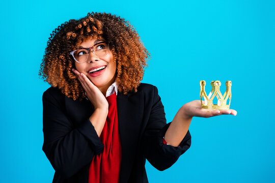 Young professional woman holding a golden crown, smiling confidently and playfully as she imagines success and leadership