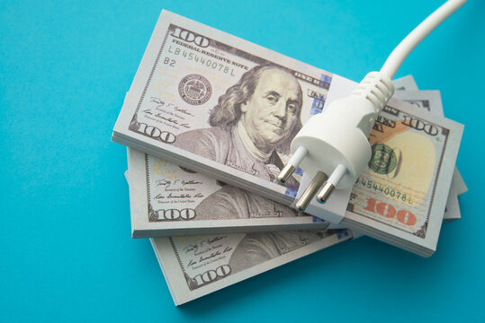 Electrical plug on heap US banknotes with blue background. Electricity bill prices increase, energy crisis, home or business financial management and planning, expense budget control concept.
