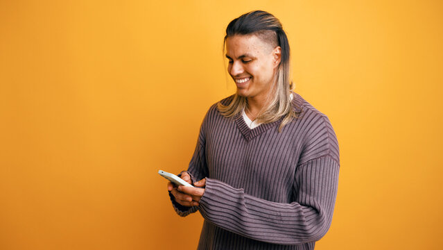 Hispanic man happy texting on his phone, wearing a comfy sweater in a studio with a vibrant yellow background