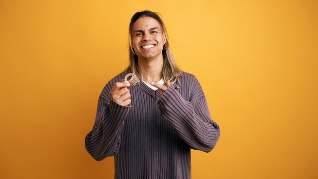 Happy latino man smiling, holding a clear dental aligner, and pointing to it, promoting orthodontics and a healthy smile