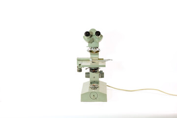 Vintage optical microscope photographed from the front showing binocular eyepieces, revolving objective turret and integrated lighting. Suitable for concepts of laboratory research, biology, medicine  © Max