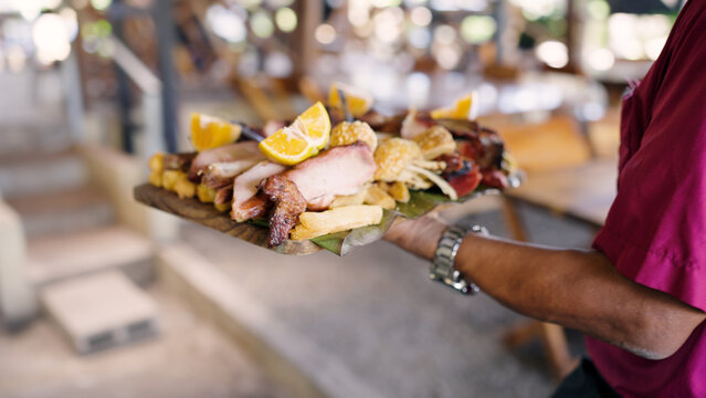Person serving a traditional Latin American mixed meat platter with yuca fries, chicharron, and citrus fruit