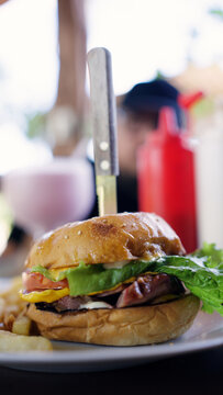 Delicious burger with bacon, cheese, lettuce, and tomato served with fries and a knife at a local Latino grill