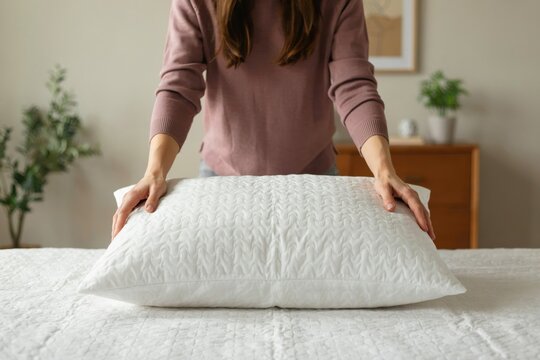A woman adjusts a soft white pillow on a bed. Use for sleep quality ads.
