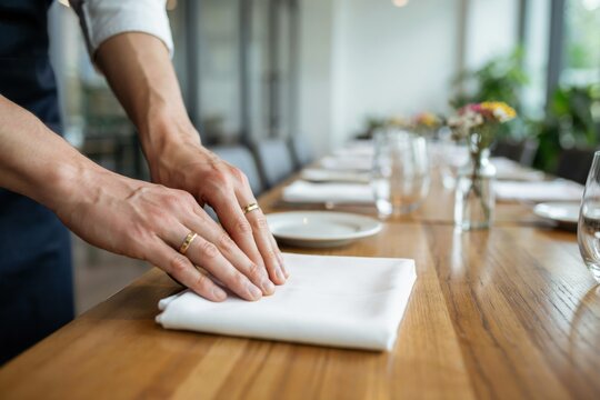 A waiter sets a white cloth on a wooden restaurant table. Service concept.