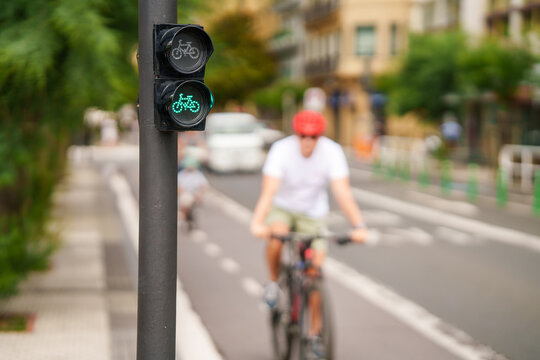 Close-up of a bicycle traffic light showing a green signal with a blurred cyclist in the background