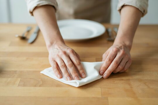 A person wipes a clean wooden table with a white napkin. Dining concept.