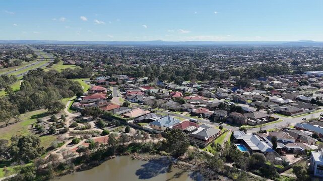 Aerial view looking across Melton in outer western Melbourne, Victoria, Australia. Residential suburban housing developments, green local parkland and a freeway stretching toward distant horizons